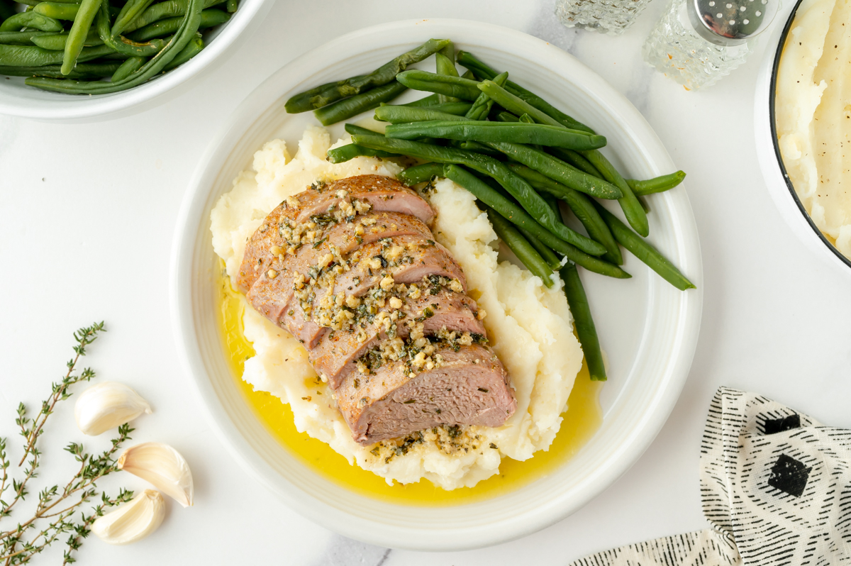 overhead shot of pork tenderloin medallions on plate with mashed potatoes and green beans