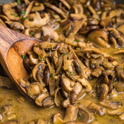 close up shot of wooden spoon in pan of cooked mushrooms