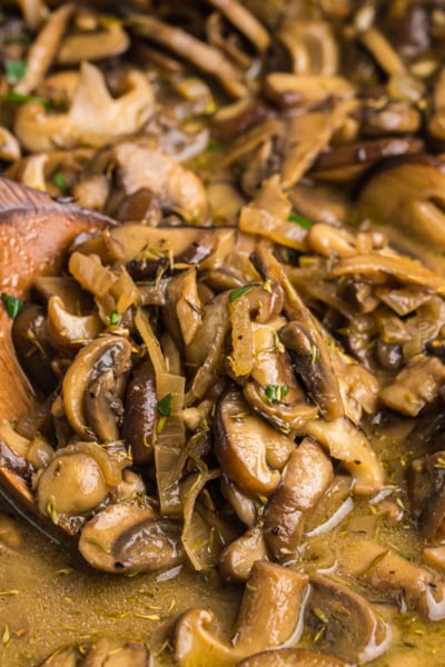close up shot of wooden spoon in pan of cooked mushrooms
