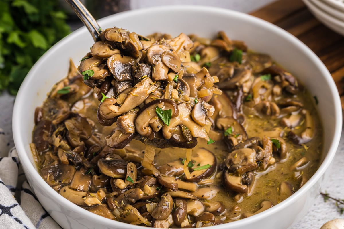 close up angled shot of serving spoon in bowl of sauteed mushrooms