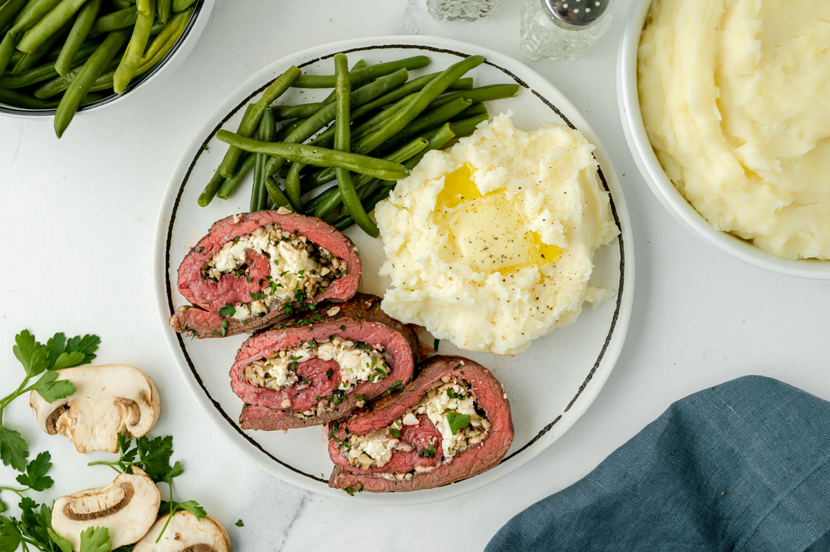 overhead shot of sliced stuffed flank steak on plate with mashed potatoes and green beans