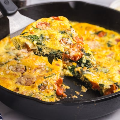 angled shot of slice of tomato spinach frittata on spatula