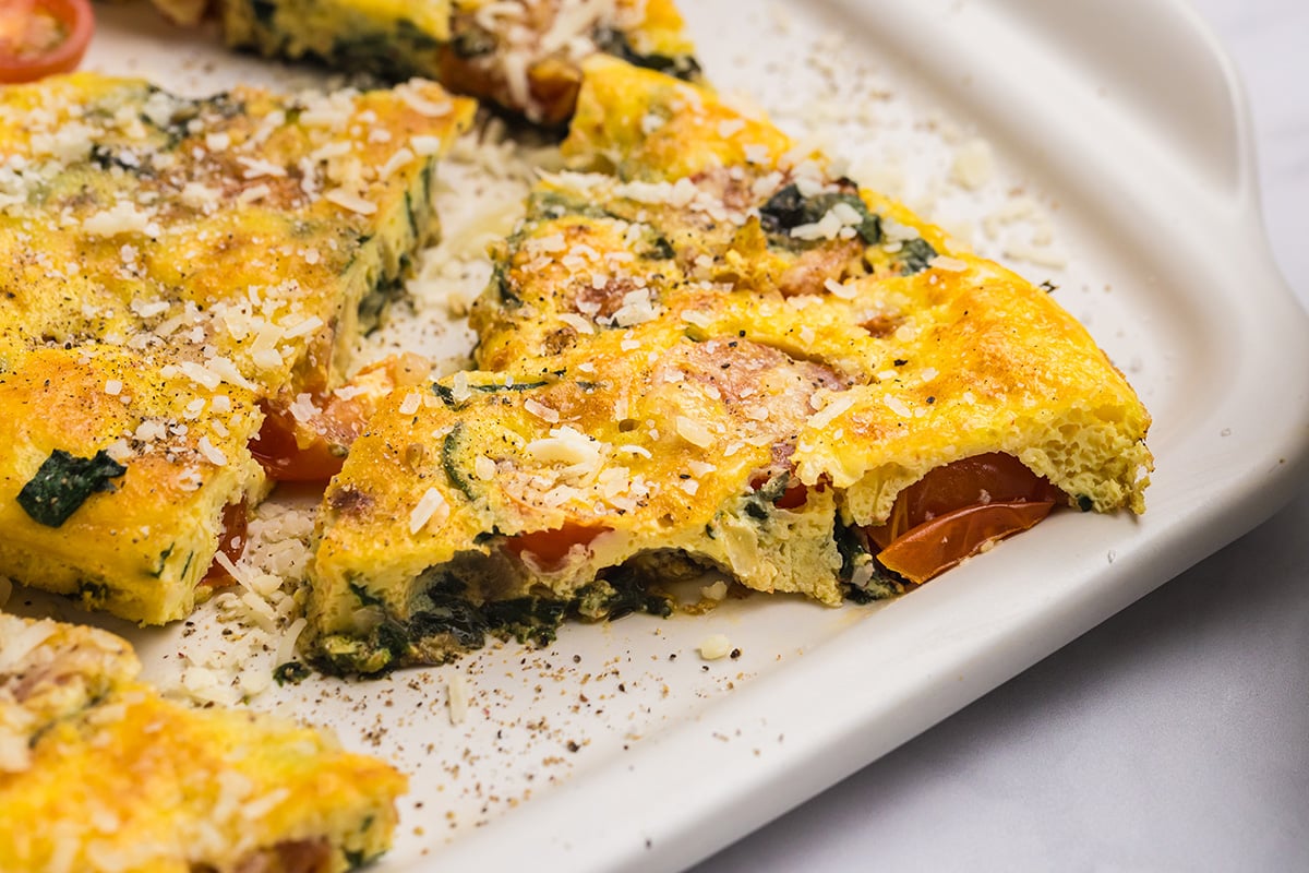 close up angled shot of slices of tomato spinach frittata on platter