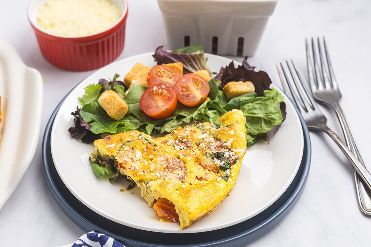 angled shot of slice of tomato spinach frittata on plate with salad