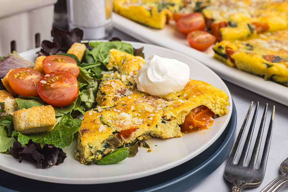 slice of tomato spinach frittata topped with sour cream on plate with side salad