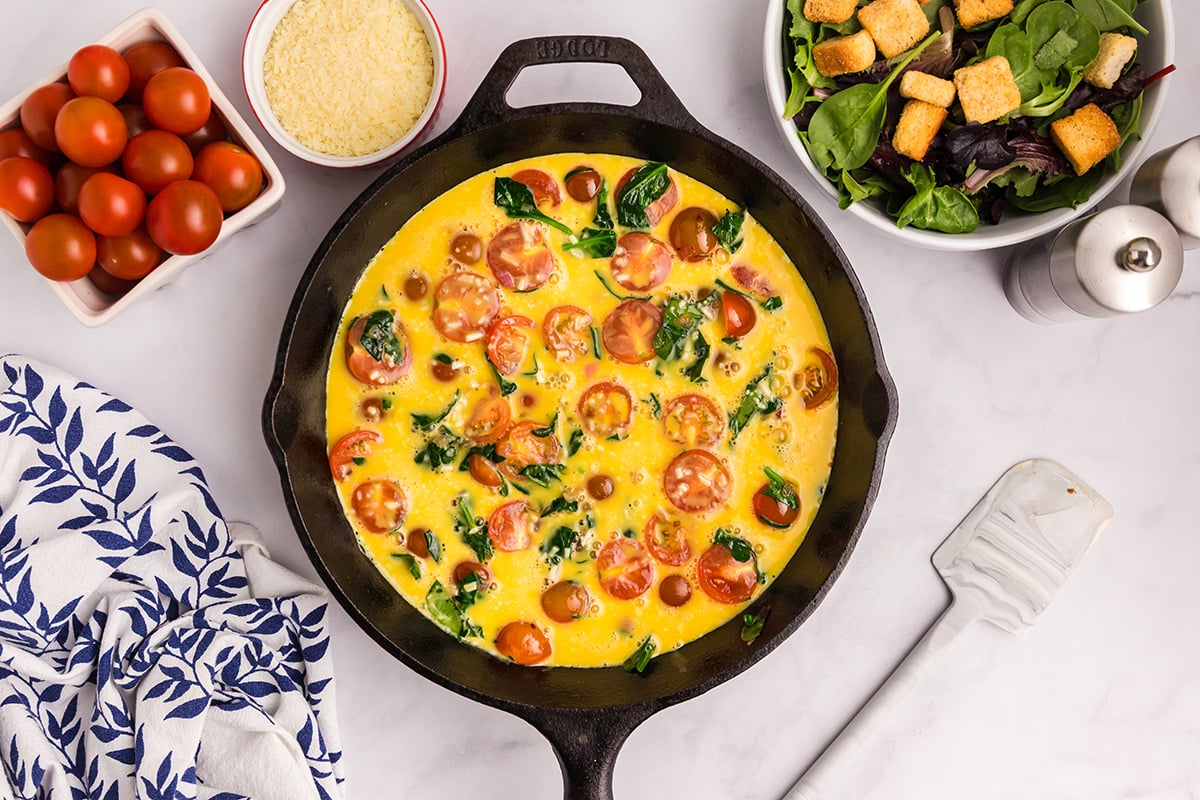 egg mixture added to veggies in cast iron skillet