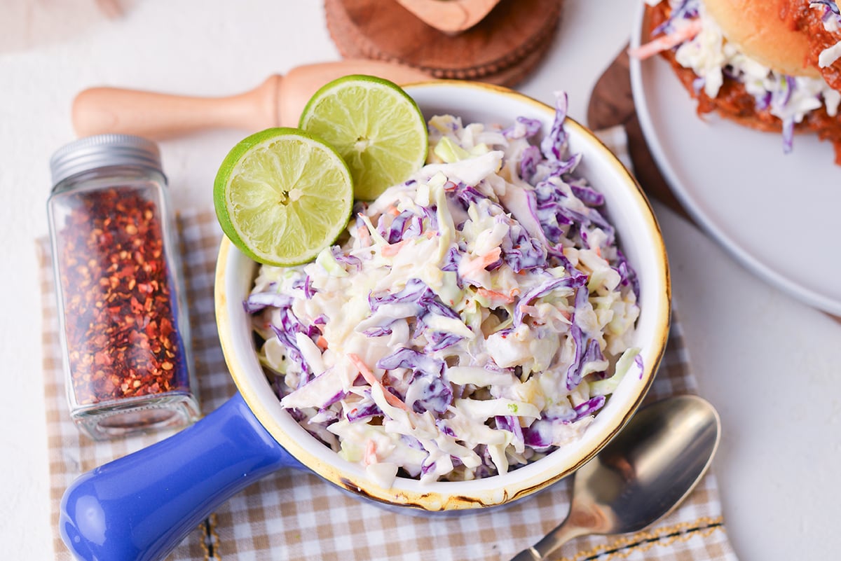 overhead shot of yogurt coleslaw in blue bowl with limes