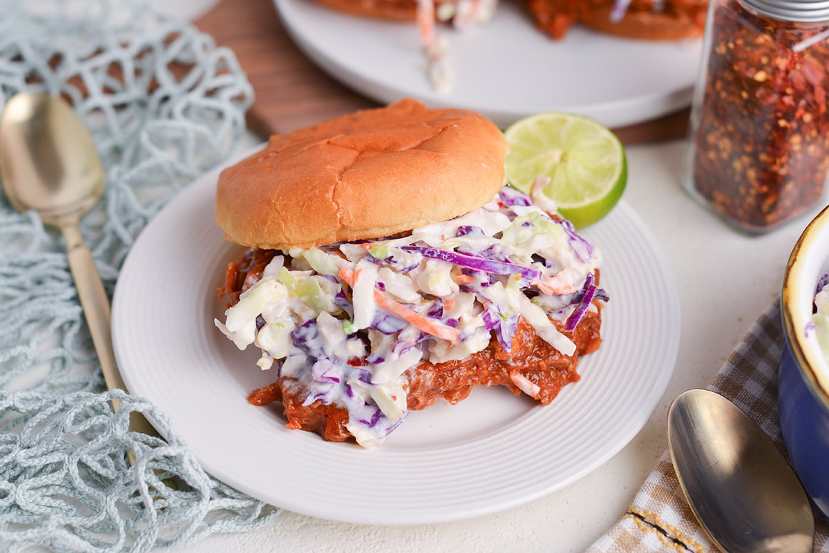 angled shot of pulled pork sandwich topped with coleslaw on plate