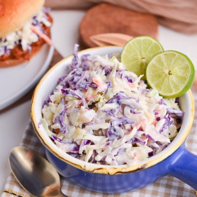 angled shot of yogurt pineapple coleslaw in blue bowl with limes