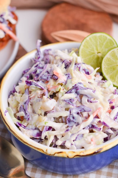 angled shot of yogurt pineapple coleslaw in blue bowl with limes