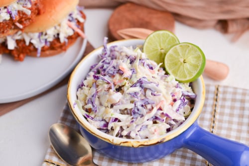 angled shot of yogurt pineapple coleslaw in blue bowl with limes
