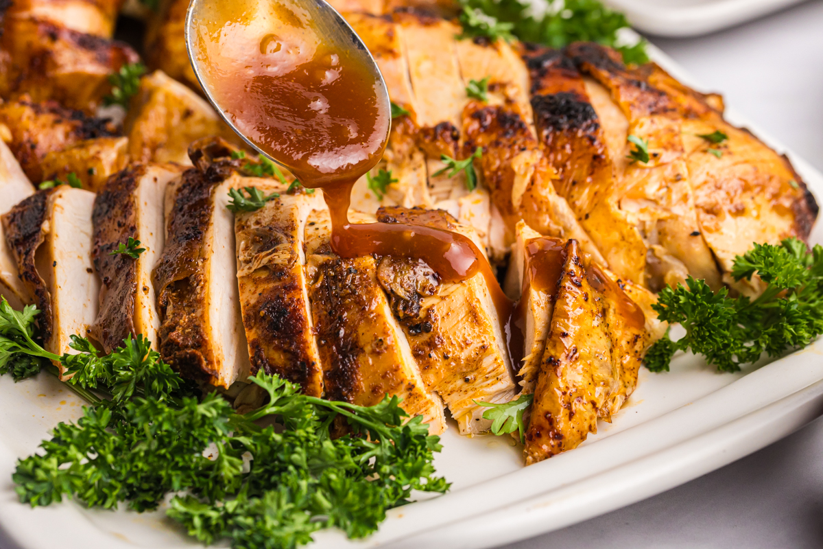 close up of spoon adding bbq sauce to sliced chicken