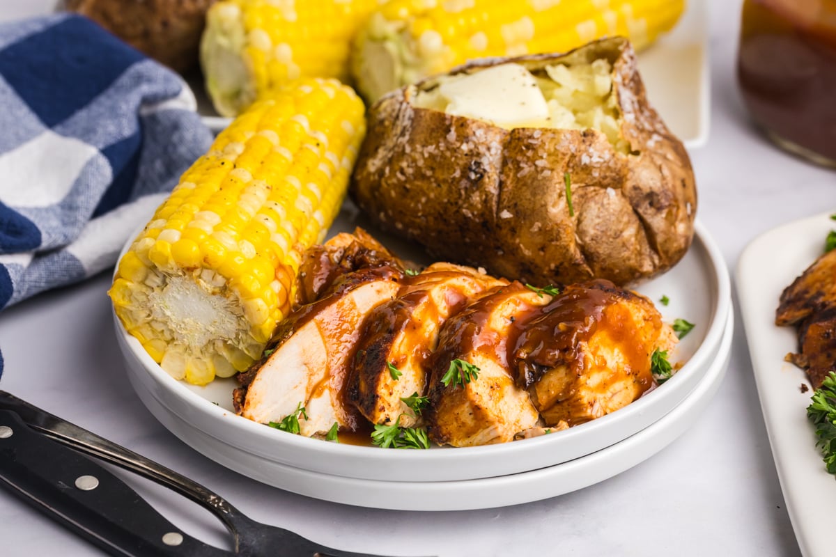 angled shot of sliced chicken on plate with corn and baked potato