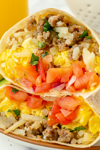 angled shot of two breakfast burrito halves on plate with fruit