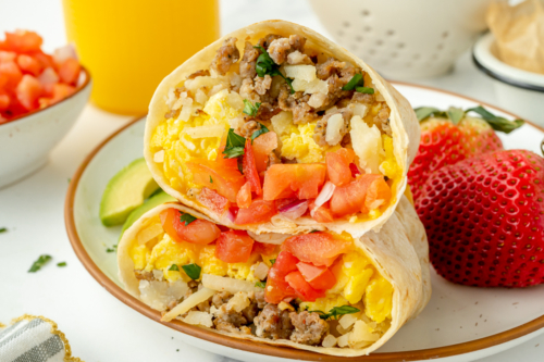 angled shot of two breakfast burrito halves on plate with fruit