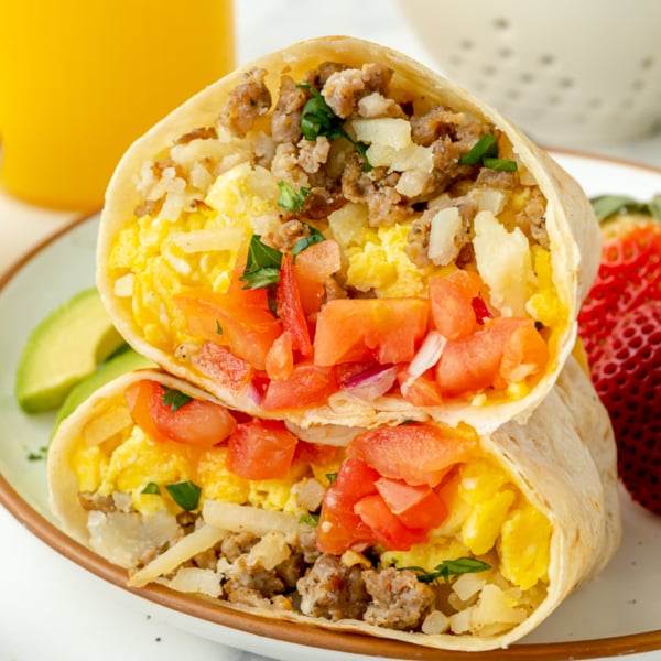 angled shot of two breakfast burrito halves on plate with fruit