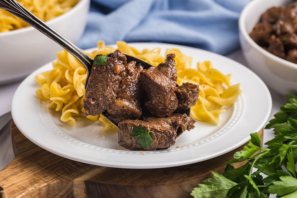spoon adding steak tips to plate of noodles