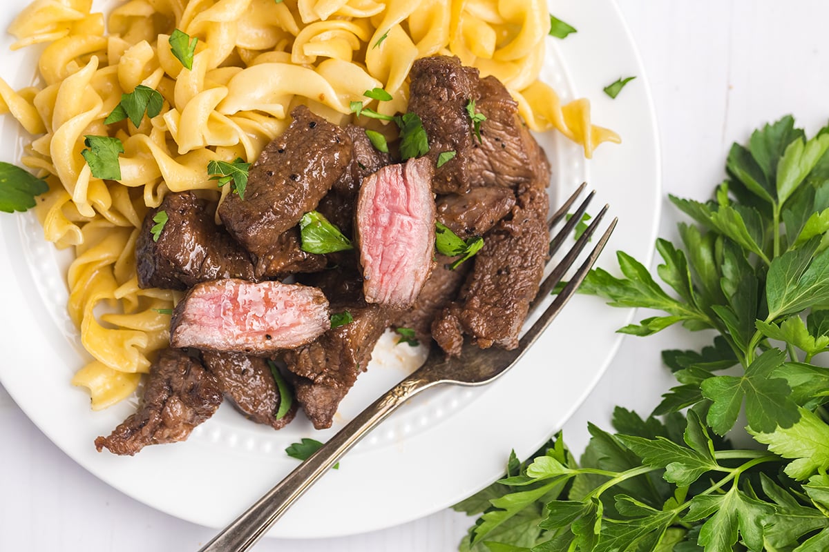 overhead shot of steak tips cut in half with noodles on a plate