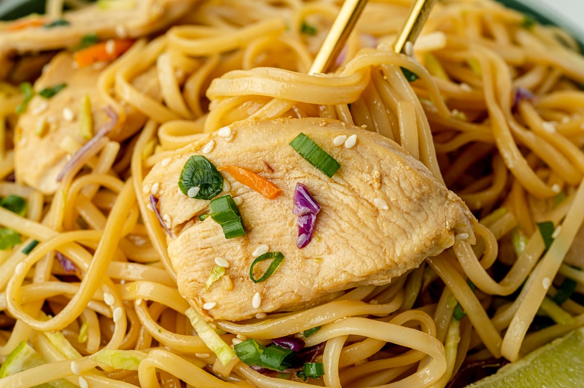 close up of bite of chicken stir fry rice noodles in chopsticks