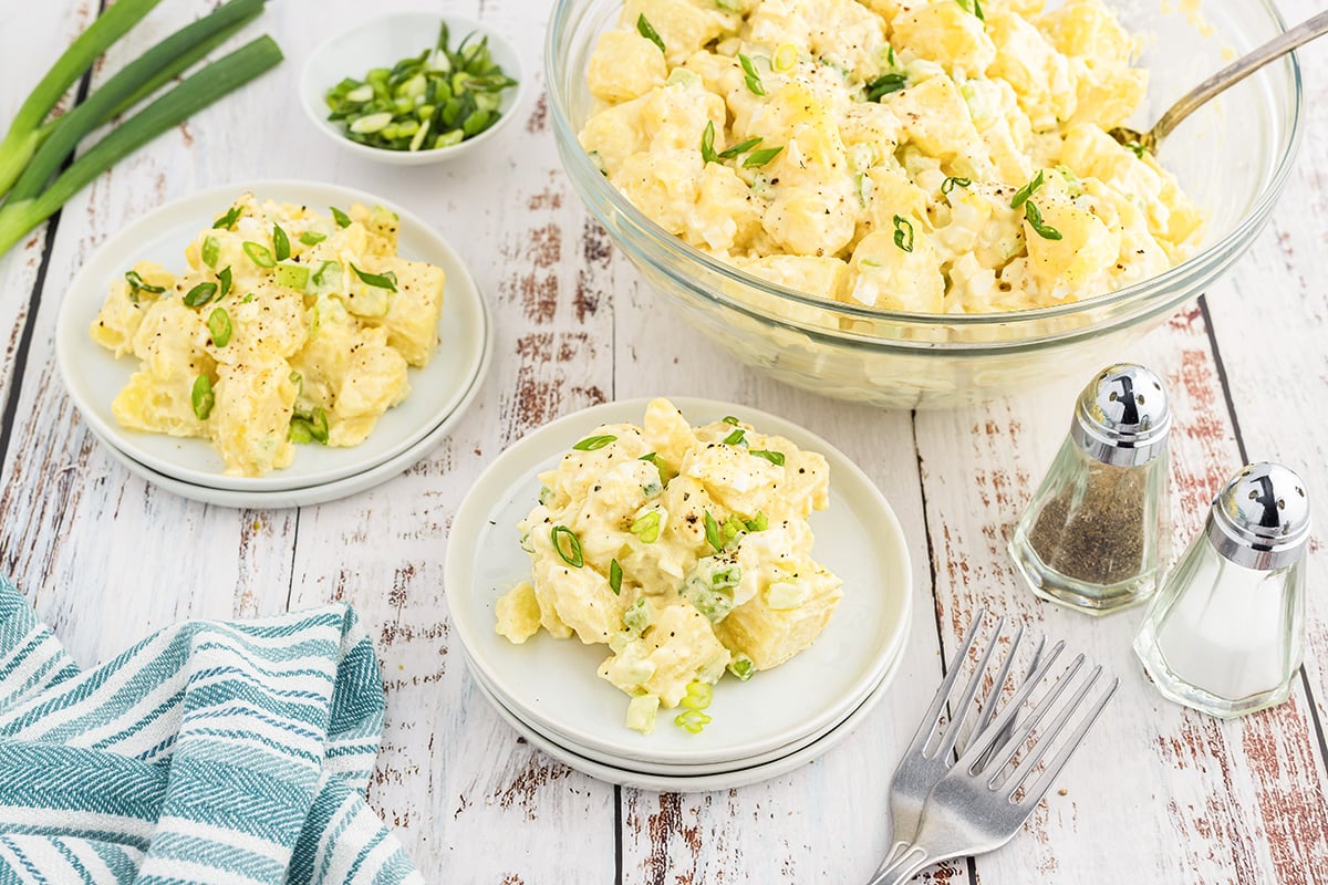 angled shot of classic potato salad in bowl and on plates