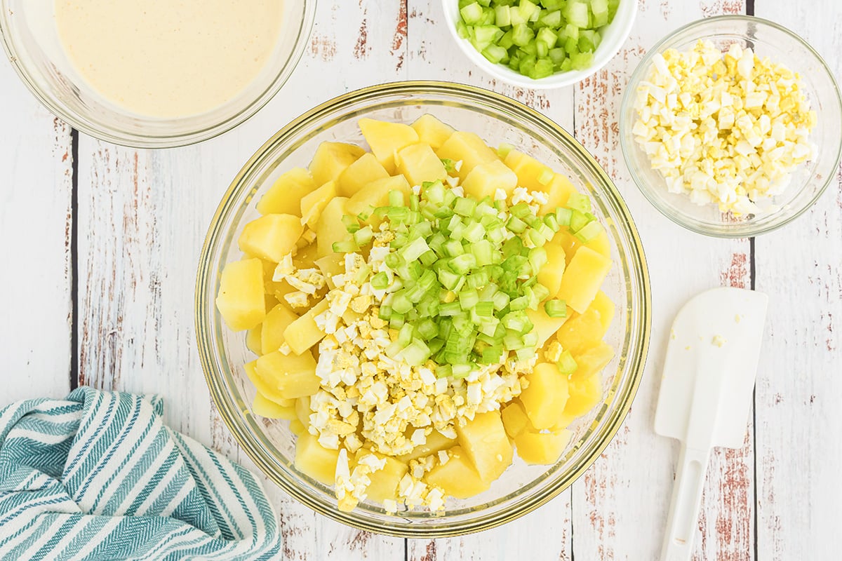 eggs and celery added to bowl of potatoes