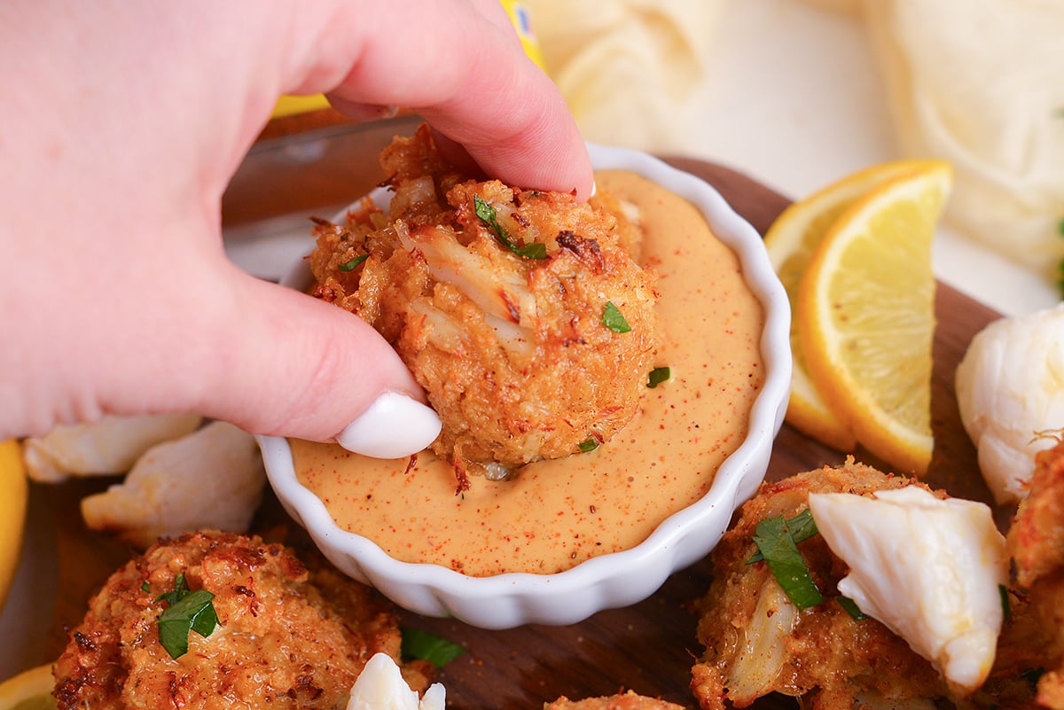 hand dipping crab ball into sauce