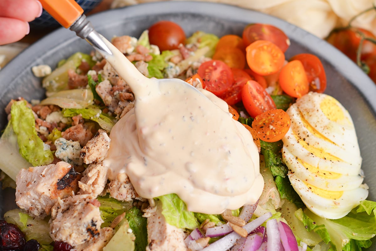 spoon adding dressing to salad