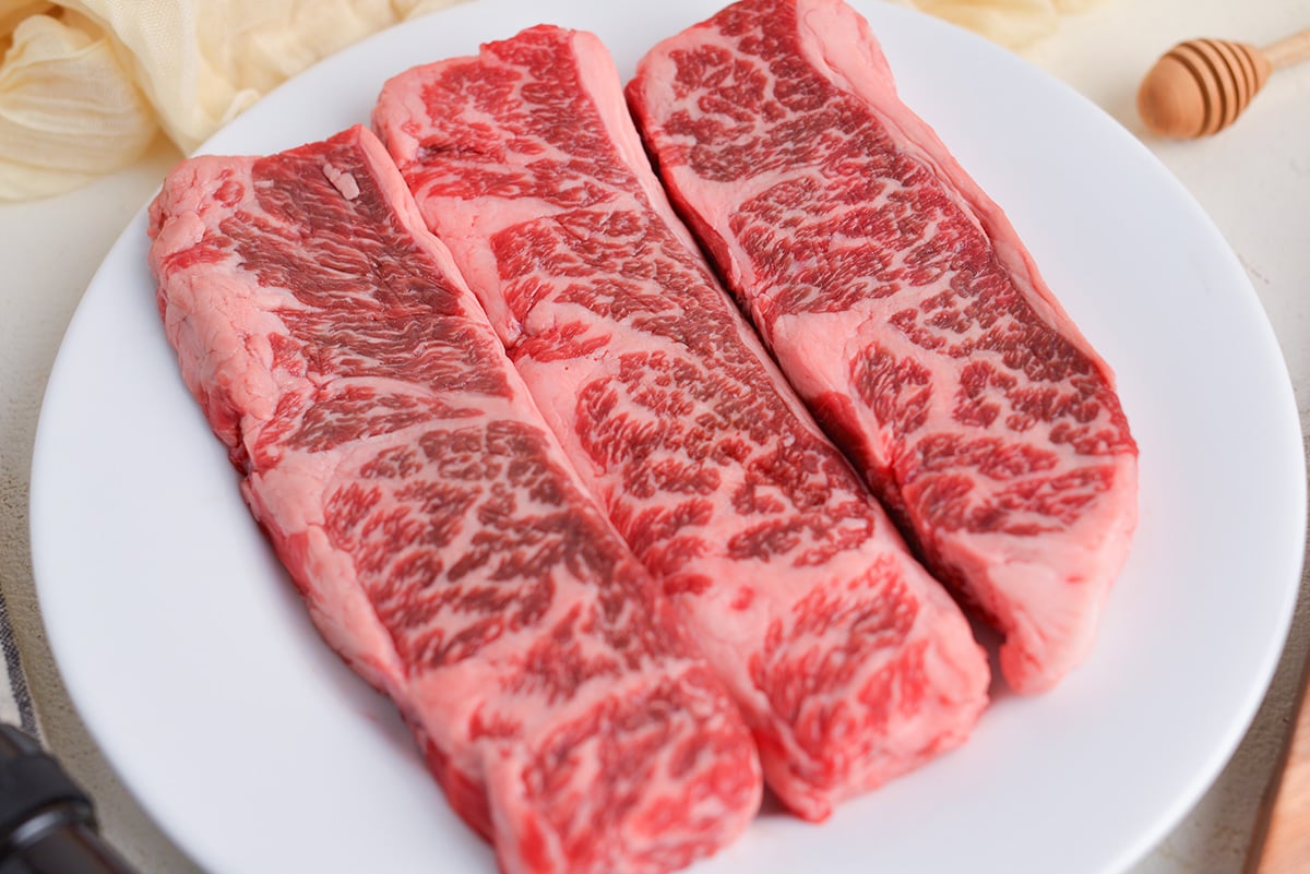 close up angled shot of three raw steaks on plate