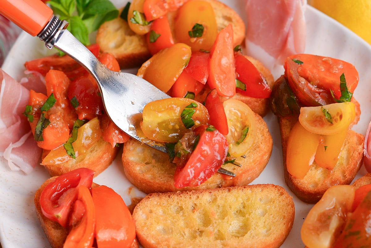 fork adding tomatoes to crostini