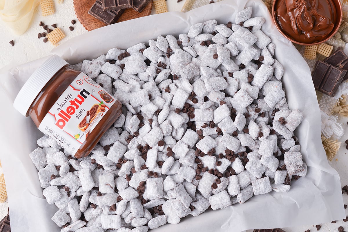 jar of nutella on baking sheet of nutella puppy chow with chocolate chips
