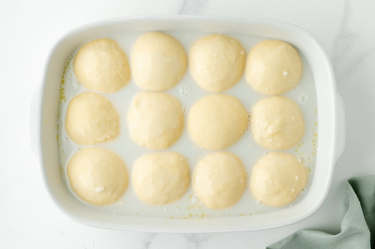 overhead shot of roll dough balls in baking dish with coconut sauce
