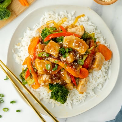 overhead shot of plate of pork stir fry over rice with chopsticks
