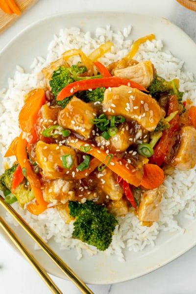 overhead shot of plate of pork stir fry over rice with chopsticks