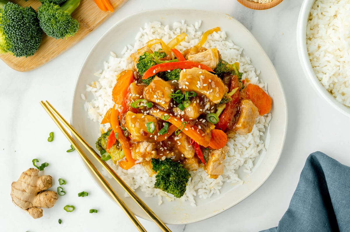 overhead shot of plate of pork stir fry over rice with chopsticks