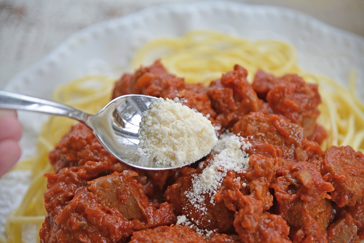 spoon adding parmesan cheese to plate of homemade spaghetti and meatballs