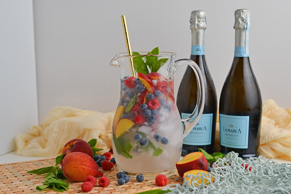 straight on shot of pitcher of sangria with two bottles of prosecco