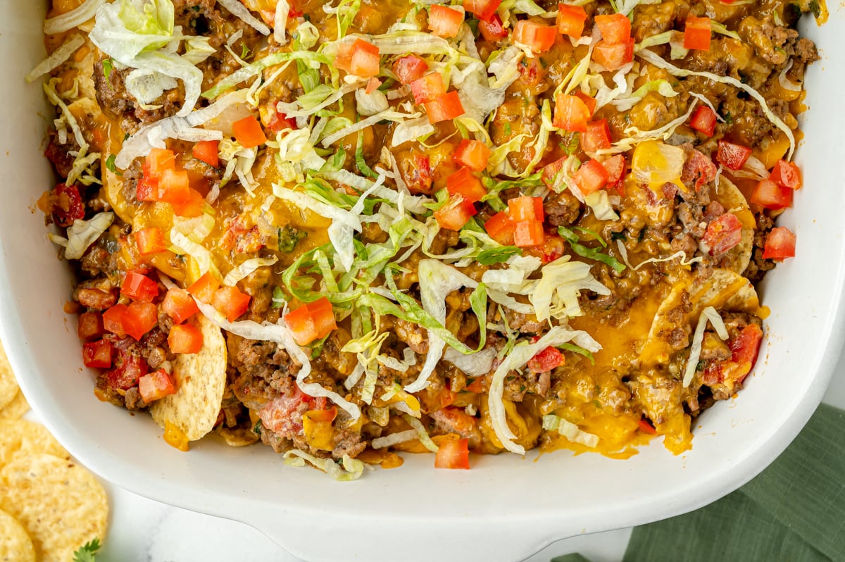 overhead shot of half of taco bake casserole topped with lettuce and tomatoes