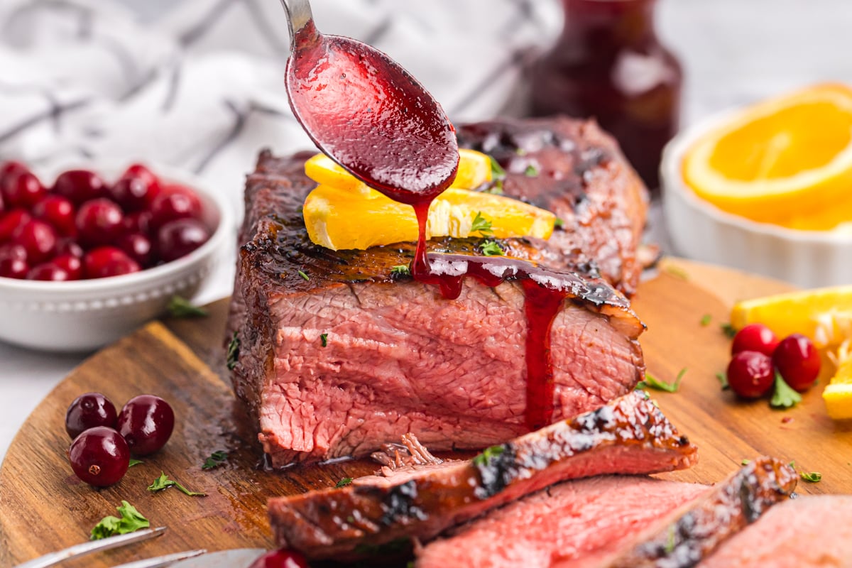 spoon adding cranberry glaze to sliced roast