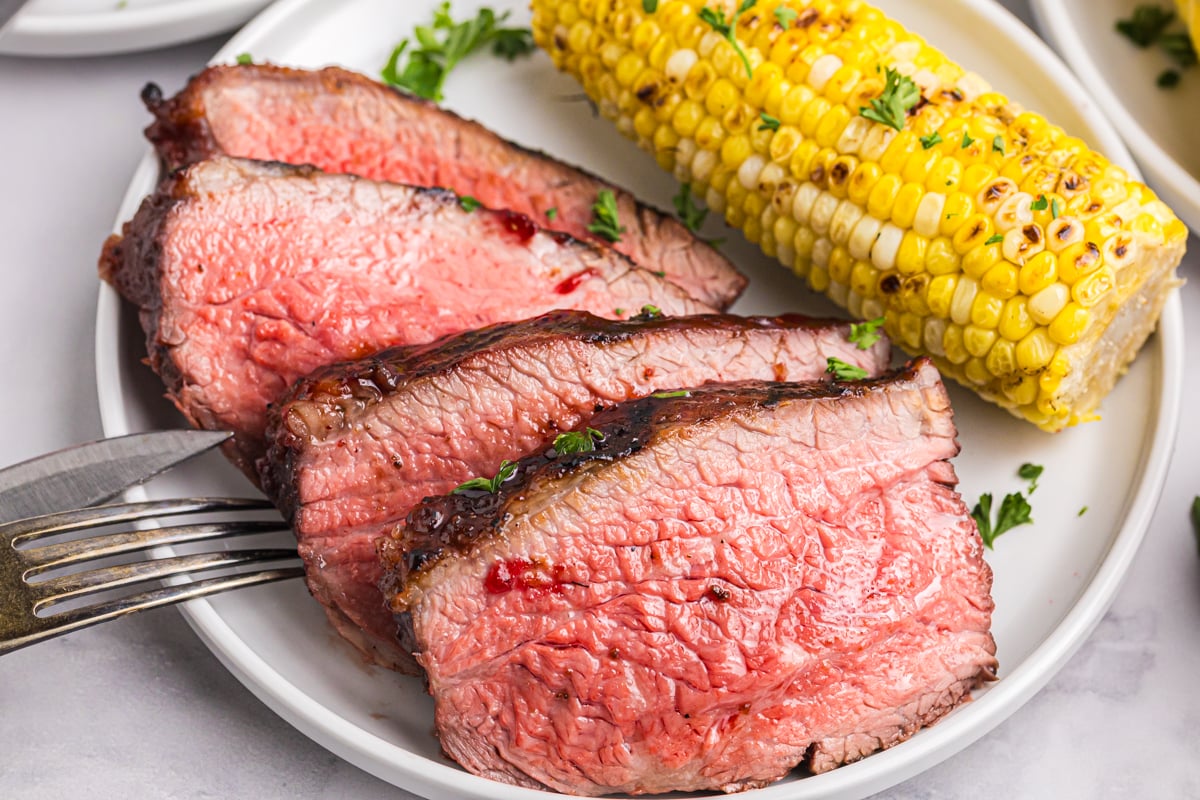 close up angled shot of sliced tri-tip roast on plate with corn