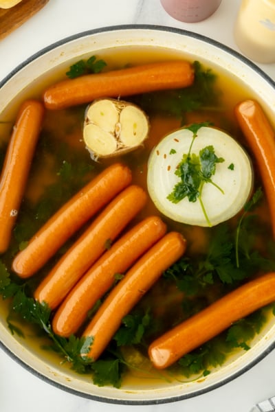 overhead shot of hot dogs in pot of water with seasonings
