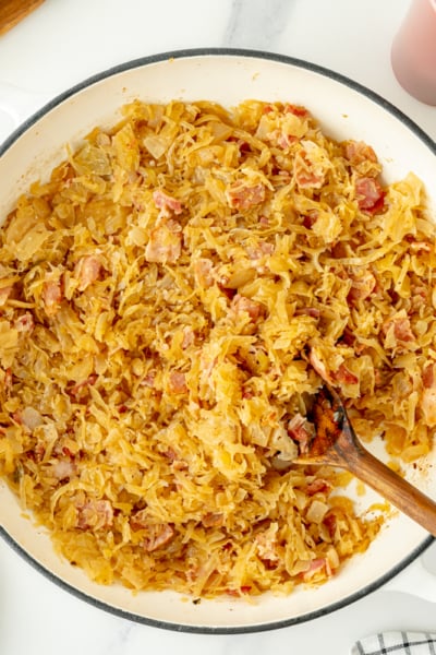 overhead shot of beer and bacon sauerkraut in pan with wooden spoon