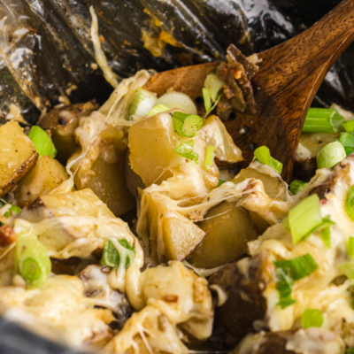 angled shot of wooden spoon in slow cooker cheesy potatoes