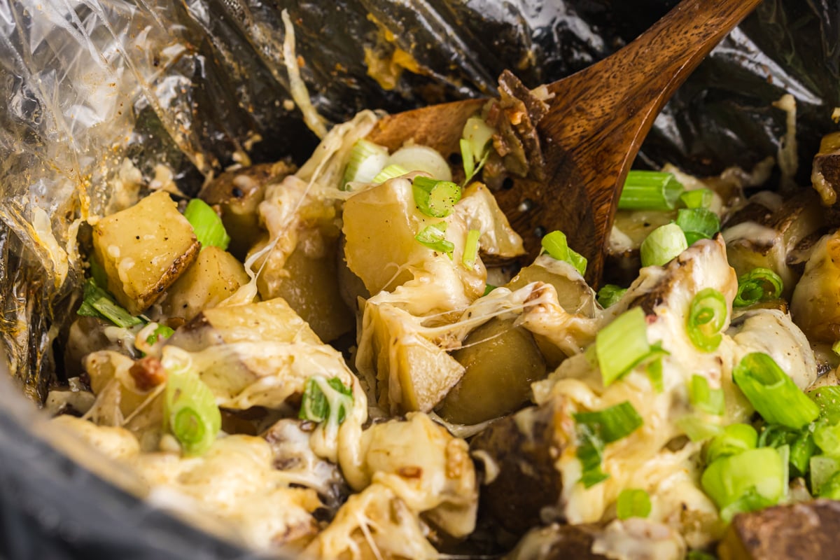 angled shot of wooden spoon in slow cooker cheesy potatoes