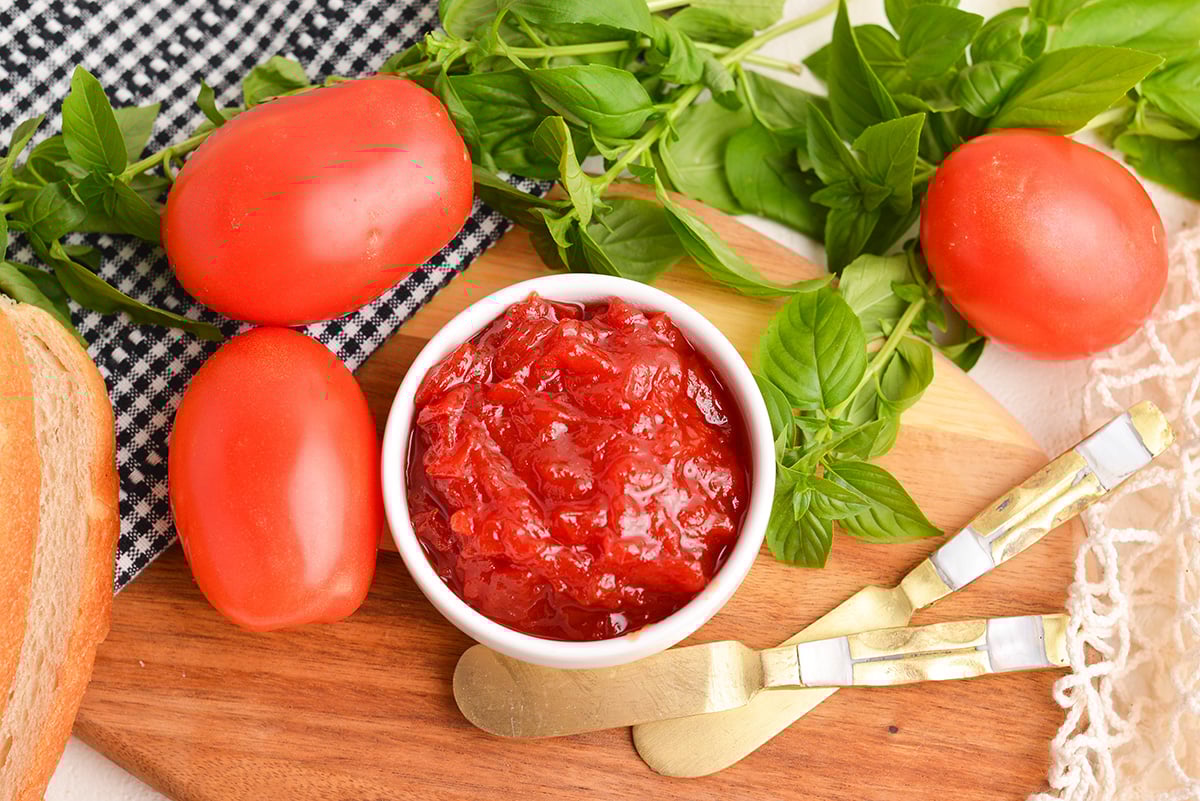 overhead shot of bowl of tomato jam on board with tomatoes and knives