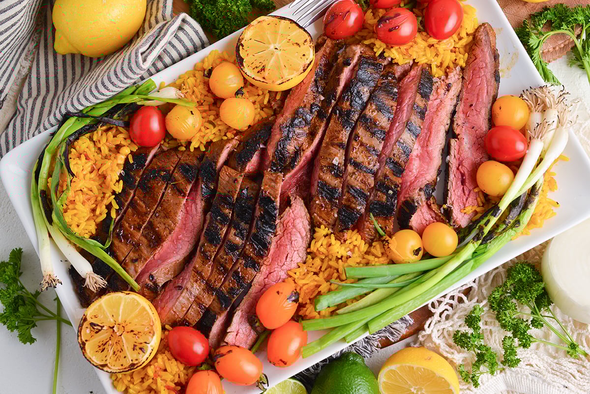 overhead shot of sliced carne asada on platter with tomatoes and rice