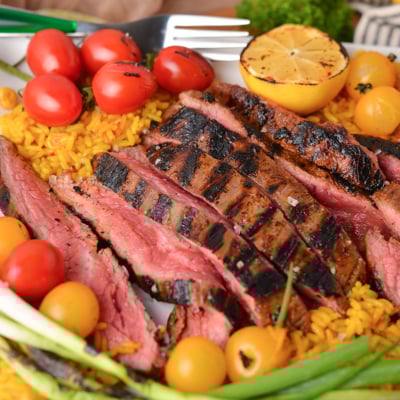 angled shot of sliced carne asada on plate with rice and tomatoes