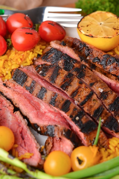 angled shot of sliced carne asada on plate with rice and tomatoes