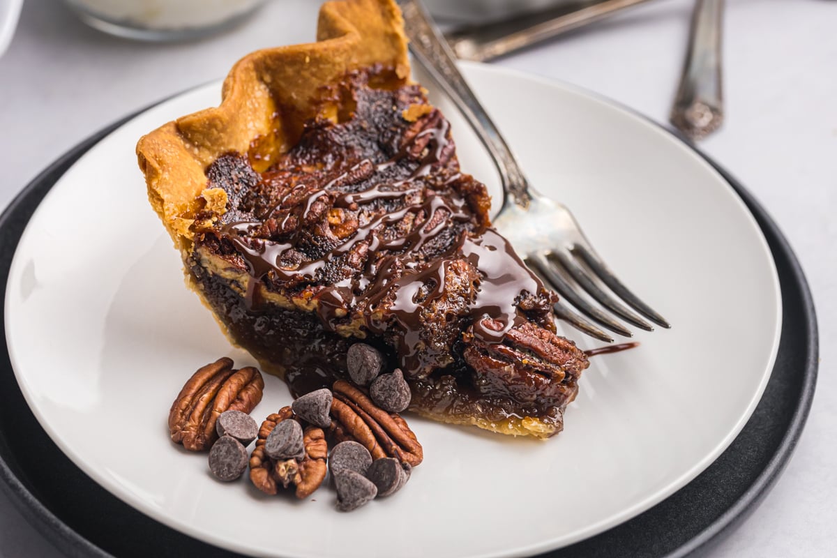 slice of gooey chocolate pecan pie on plate with pecans and chocolate chips