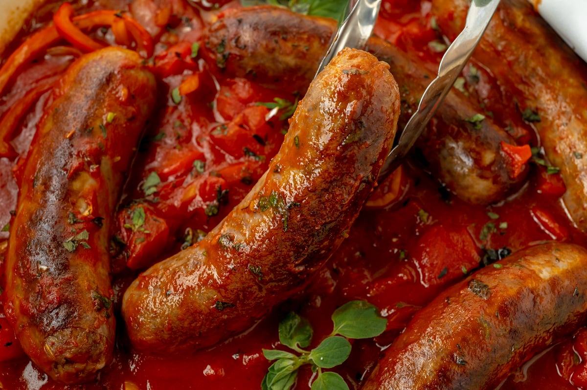 tongs holding italian sausage and peppers