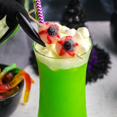creepy hand adding eyeball gummies to glass of witches brew